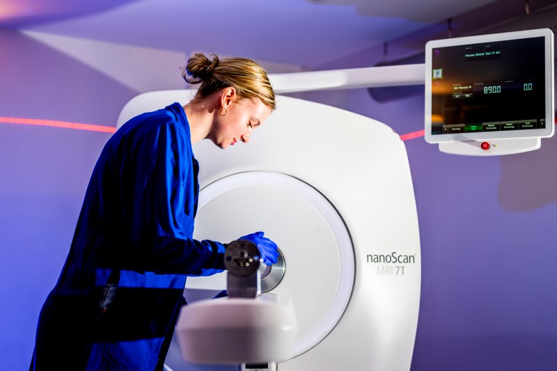 A woman with blonde hair in a blue grown operates a PET scanner.