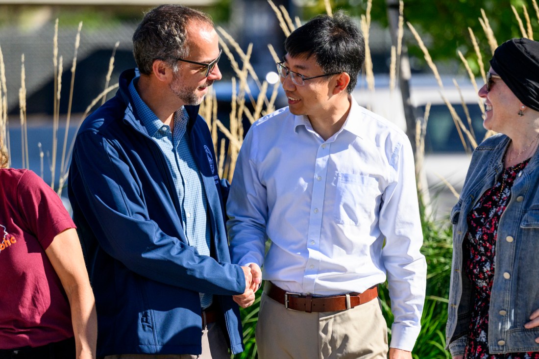Two men shake hands and smile while talking with another attendee during the City of Boston Air Grant event in Allston, Massachusetts.