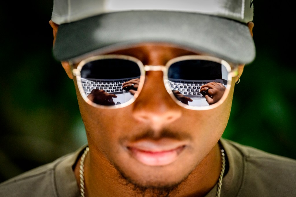 Close-up of Stephen Jacques, a Northeastern finance student, with a laptop keyboard reflected in his sunglasses as he works outside Snell Engineering Center.