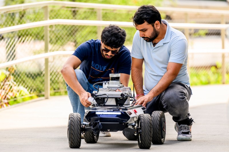Two students work on a robot outside.