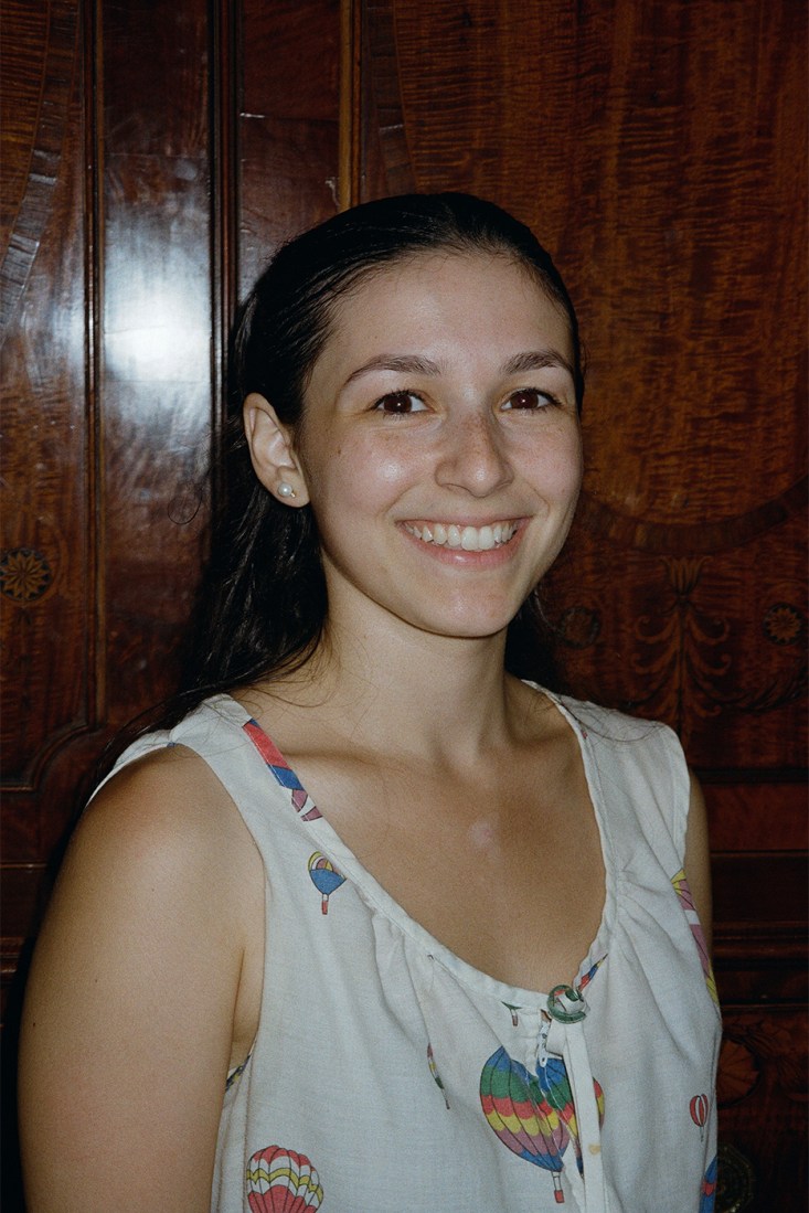Brooke Di Spirito, a white woman with black hair, depicted smiling against a wooden backdrop.