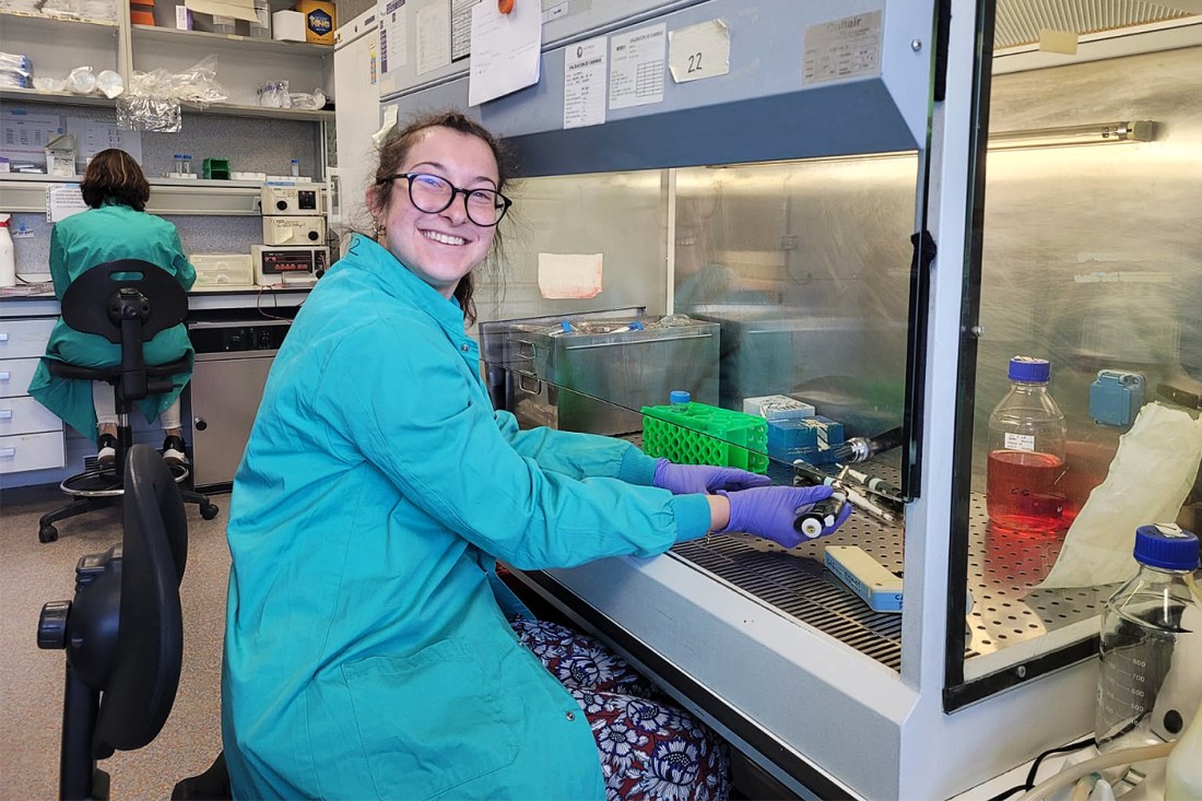 Federica Ciummo working in the lab, wearing a teal lab coat and pants with a white floral design.