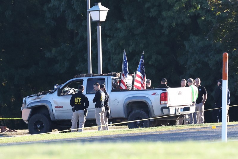 A far shot of law enforcement standing next to a vehicle used to ram a church building, which contains two American flags in its back portion.