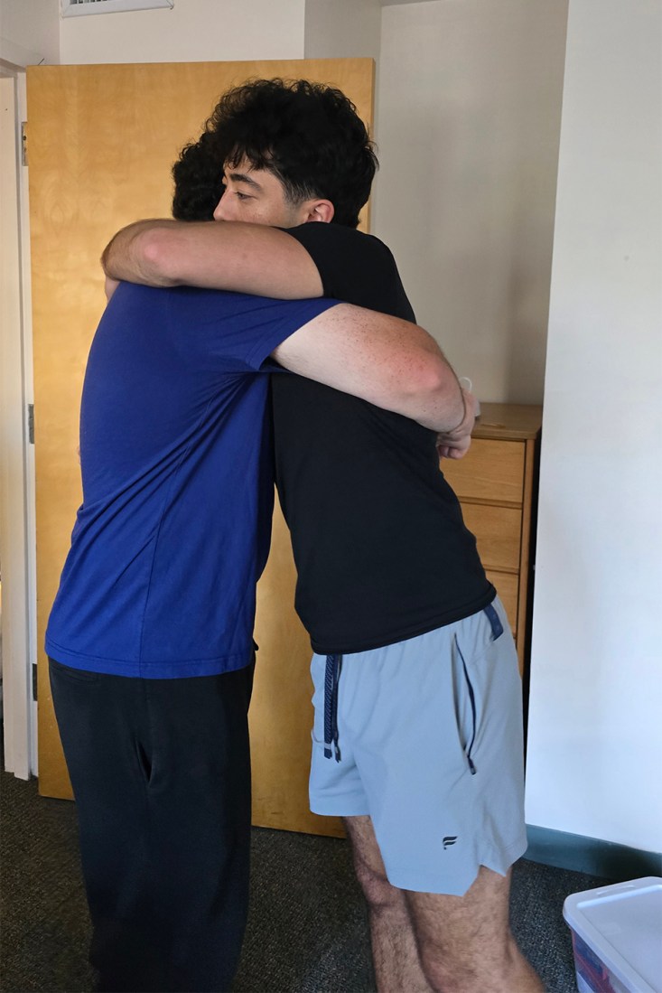 Braden and Gabriel Pelletier hugging each other in a dorm room in Oakland. 