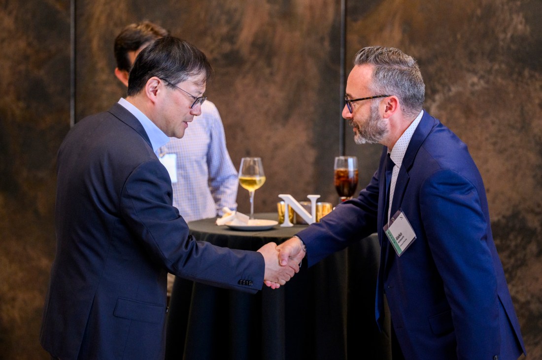 Three new faculty members, all men in suits, chat at a table, while two of them appear to shake hands.