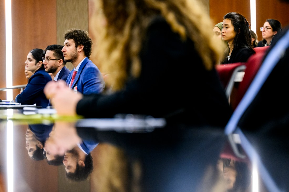Legal students dressed in suits sit at a long, reflective desk inside Northeastern's Moot Court Room.