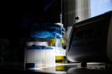 A gloved hand, protruding out of the shadows, holds up a test tube containing scientific samples.
