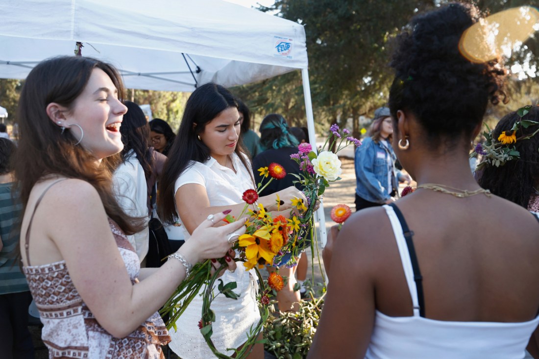 Students assembling bouquets of flowers outside next to a white tent.