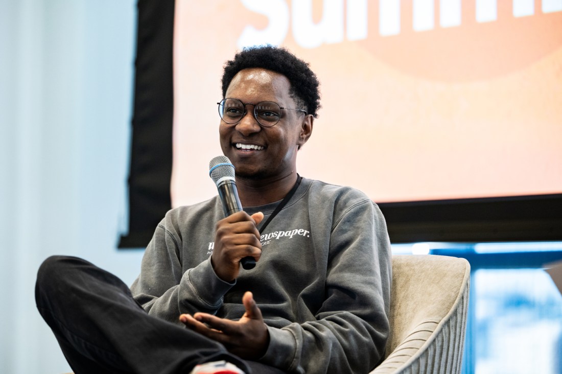 Joseph Ferguson sitting in a modern arm chair on stage, smiling and holding a microphone. 