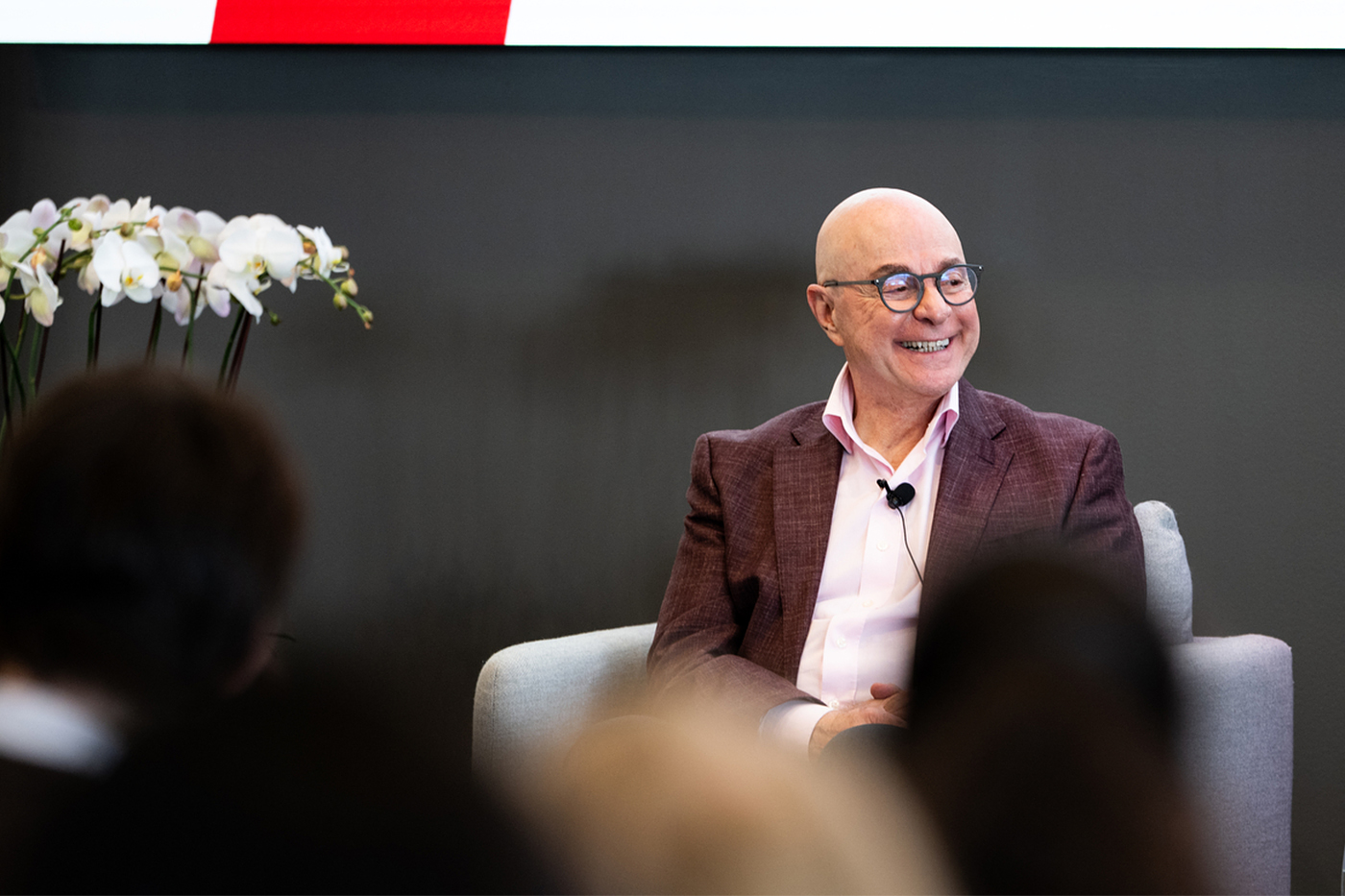 Northeastern University President Joseph E. Aoun smiles while seated onstage during a fireside chat. A small flower arrangement is visible beside him.