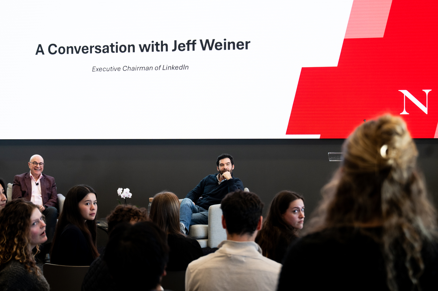 Jeff Weiner speaks on stage beside President Joseph E. Aoun during a fireside chat at Northeastern University, as audience members listen and engage in the discussion.