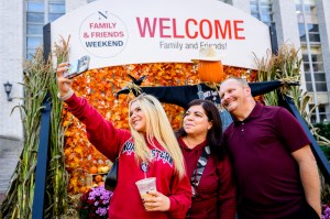 Madison McCall, a Northeastern student, takes a selfie with her parents in front of the "Family & Friends Weekend" welcome sign.