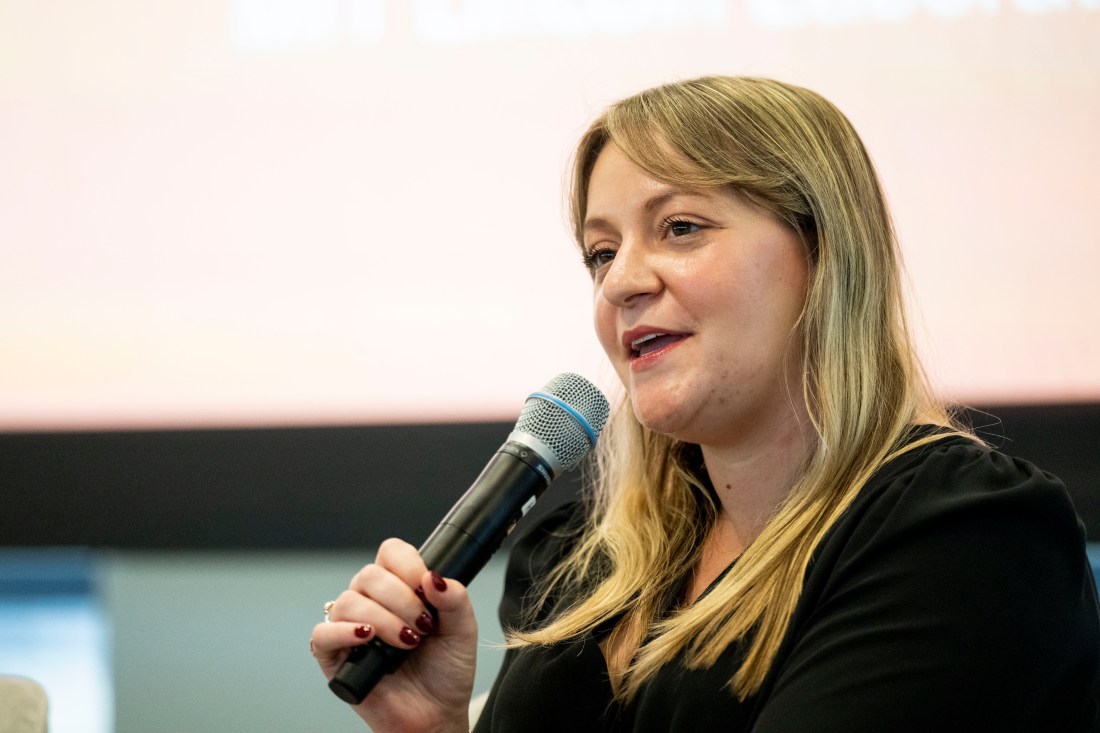 Ashley Bourque holding a microphone and speaking into it while on stage at the Social Media Summit. 