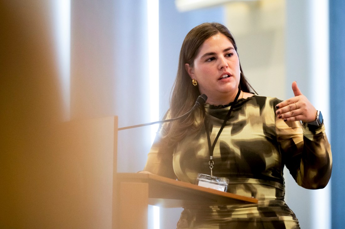Fernanda Hurtado Ortiz wearing a green patterned dress gesturing while speaking at a wooden podium on stage at the Social Media Summit. 