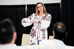 Illena Armstrong, wearing an embroidered white dress, gesturing while speaking at a training event.