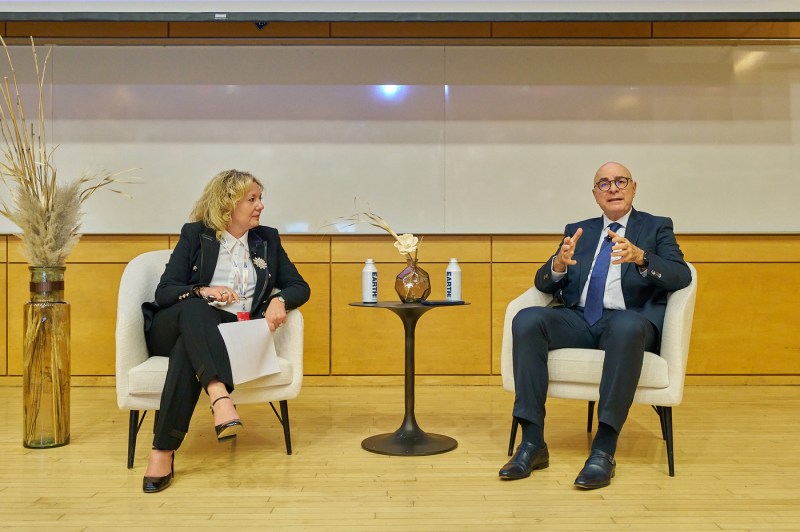 Northeastern University President Joseph E. Aoun, seated in a white chair next to Roberta Iannacito-Provenzano, gestures while speaking on stage.