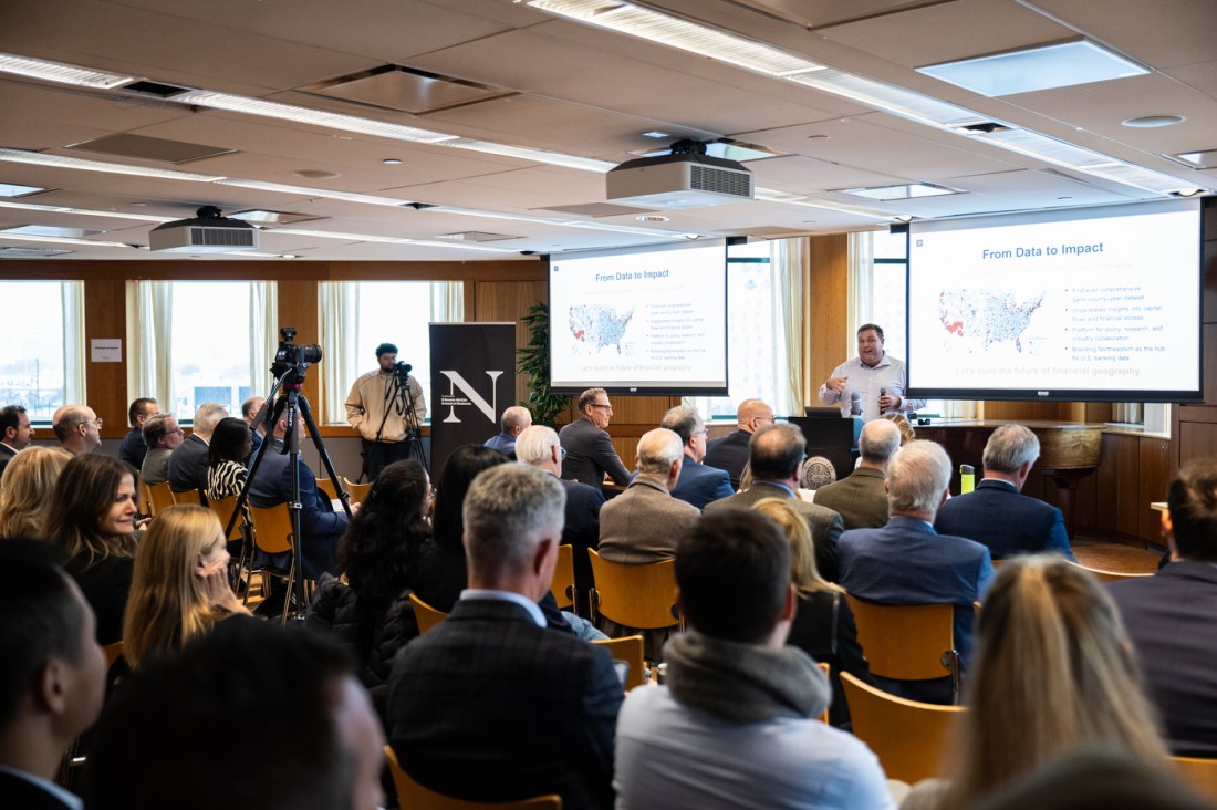 A speaker presents to an audience seated in the Alumni Center at Northeastern University, with slides projected behind him during DMSB Day.