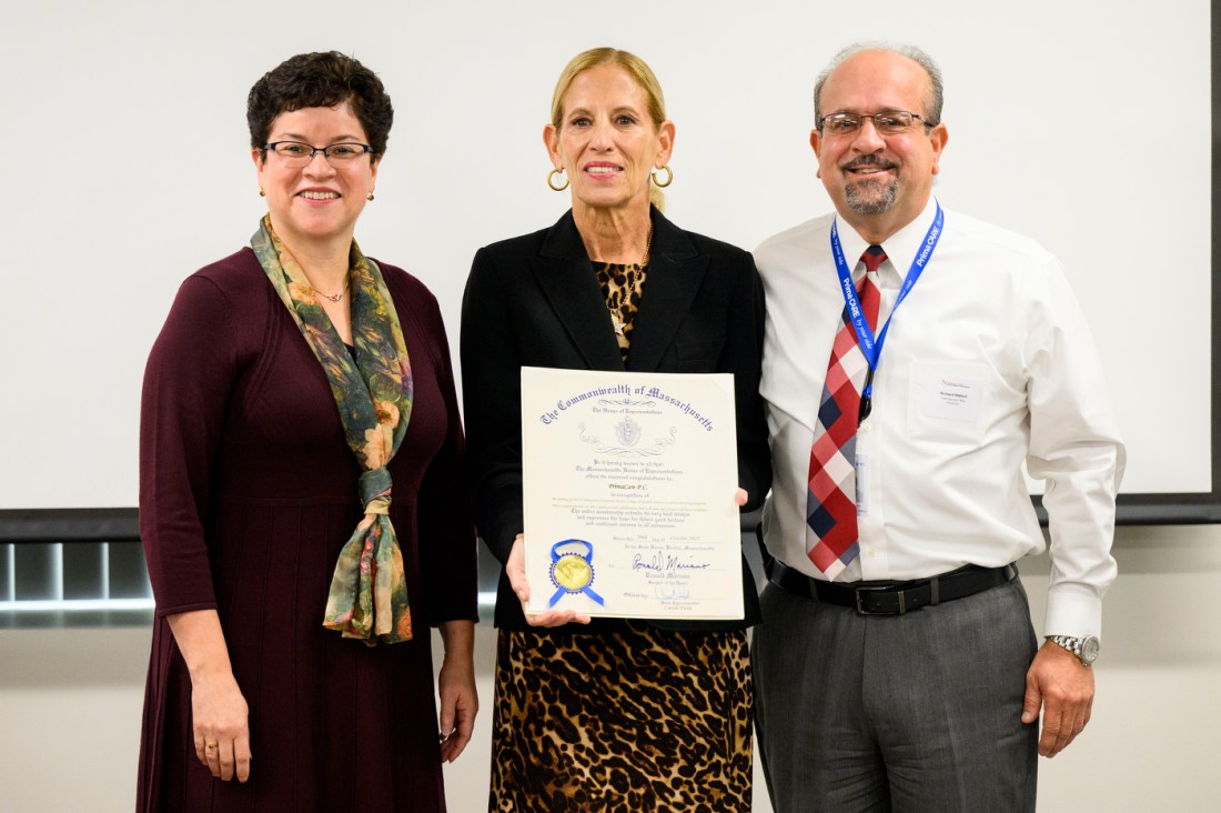 Three people stand together, posing for a photo. The person in the middle is holding a certificate. All of them are smiling. 