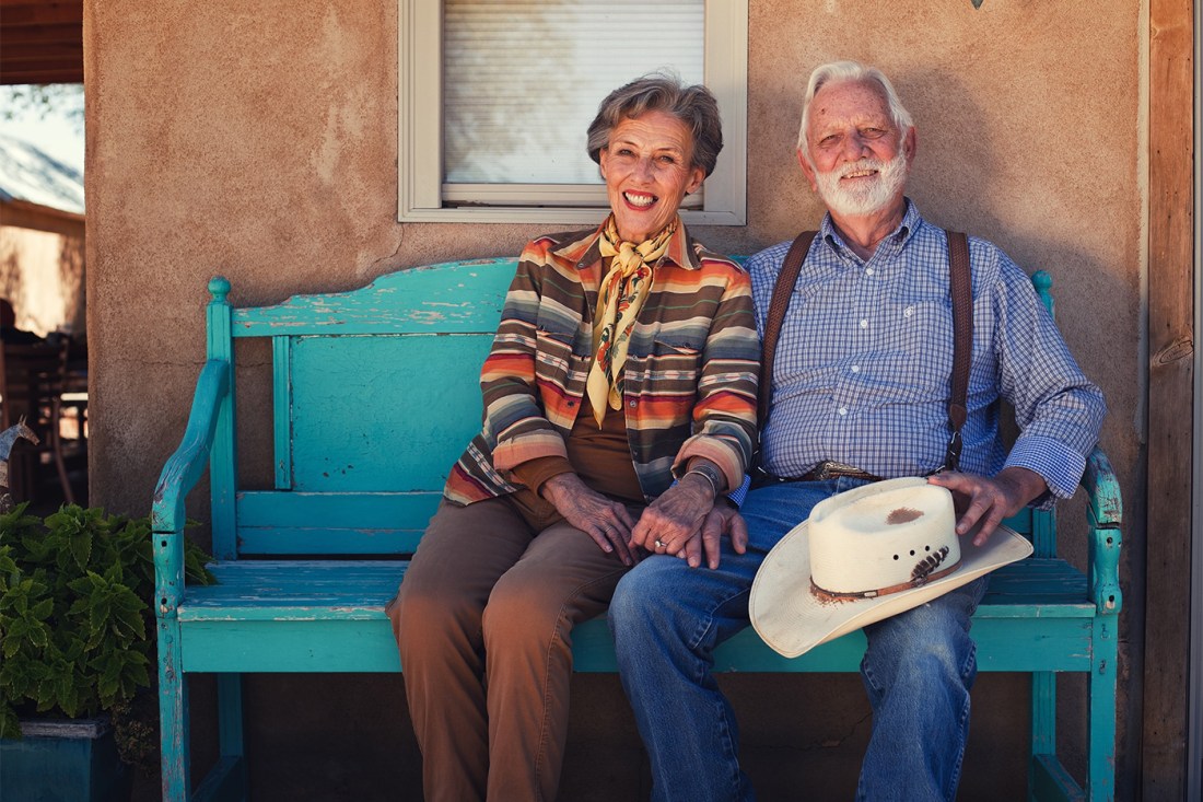 Tuda Libby Crews, CEO of Ute Creek Cattle Company, and her husband, Jack Crews, sitting on a tattered teal bench against an orange wall and smiling. 