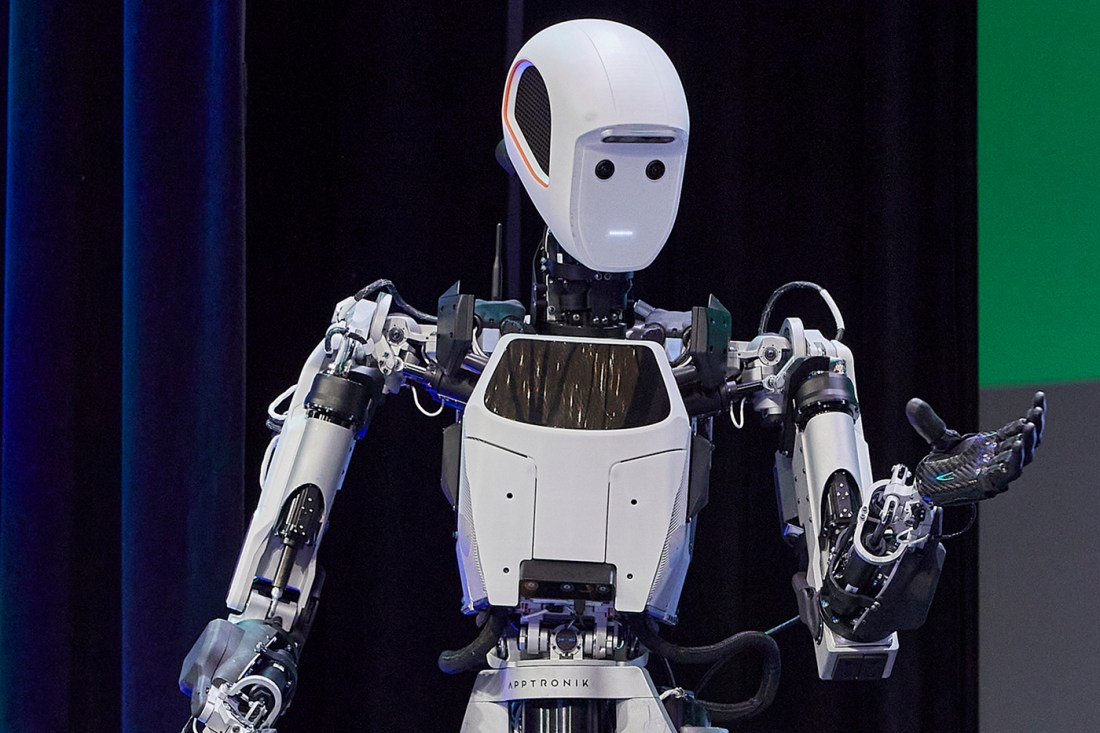 A humanoid robot with white body segments and a neutral expression gestures with a hand.