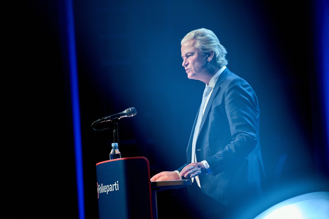 Dutch politician Geert Wilders standing at a podium and speaking during the Danish People's Party annual meeting.