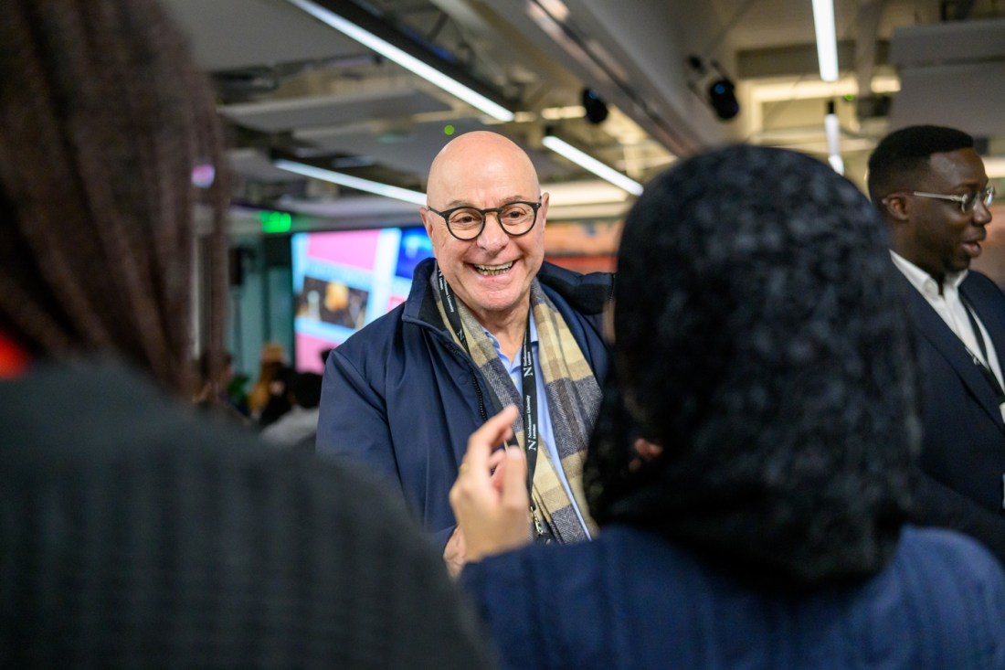 President Aoun wearing a blue jacket and scarf smiling while talking to a person standing in front of him with their back to the camera. 