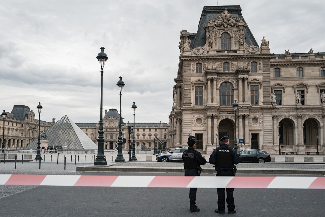 Police officers standing in front of the Louvre Museum on a cloudy day.