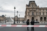 Police officers standing in front of the Louvre Museum on a cloudy day.