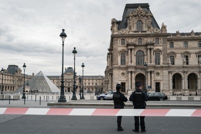 Police officers standing in front of the Louvre Museum on a cloudy day.