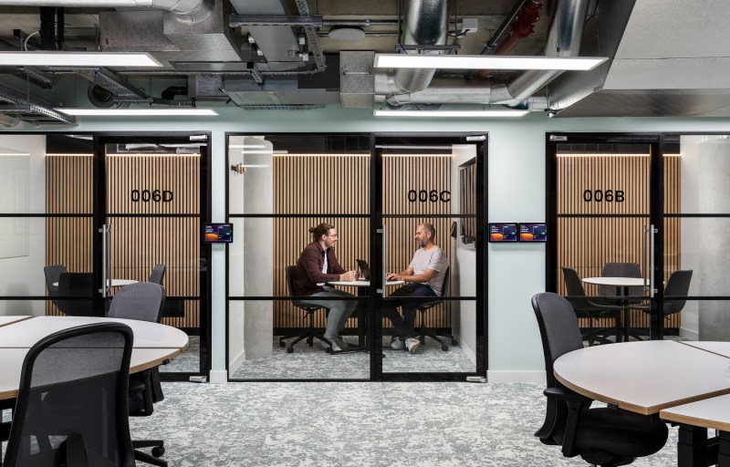 Two people sit across from each other at a small table inside a glass-walled meeting room at Northeastern University’s London startup hub, which houses 22 external businesses and provides students with hands-on work opportunities.
