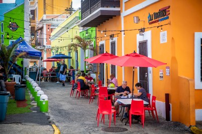 A colorful restaurant row, where diners sit outside alongside an orange building in downtown San Juan.