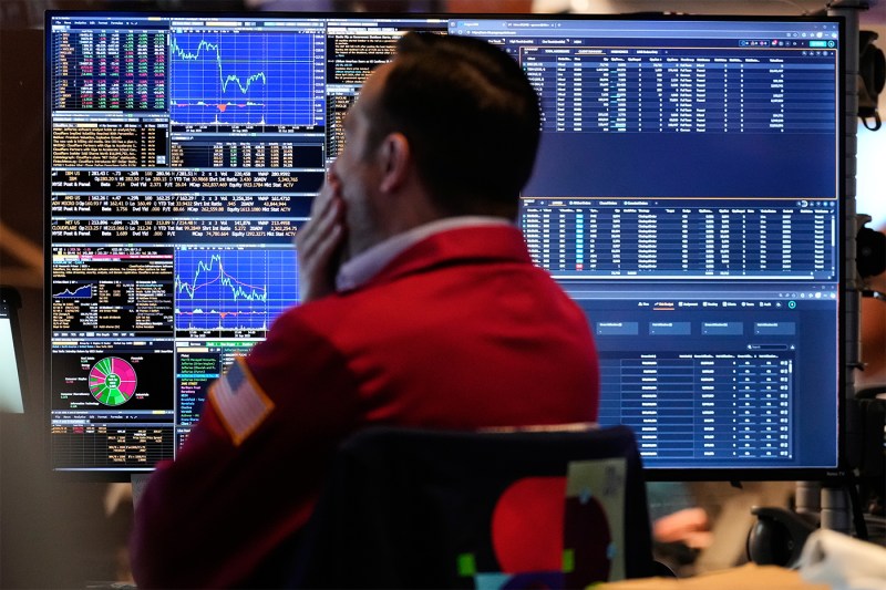 A trader wearing a dark shirt and red vest looking at financial information on his computer.